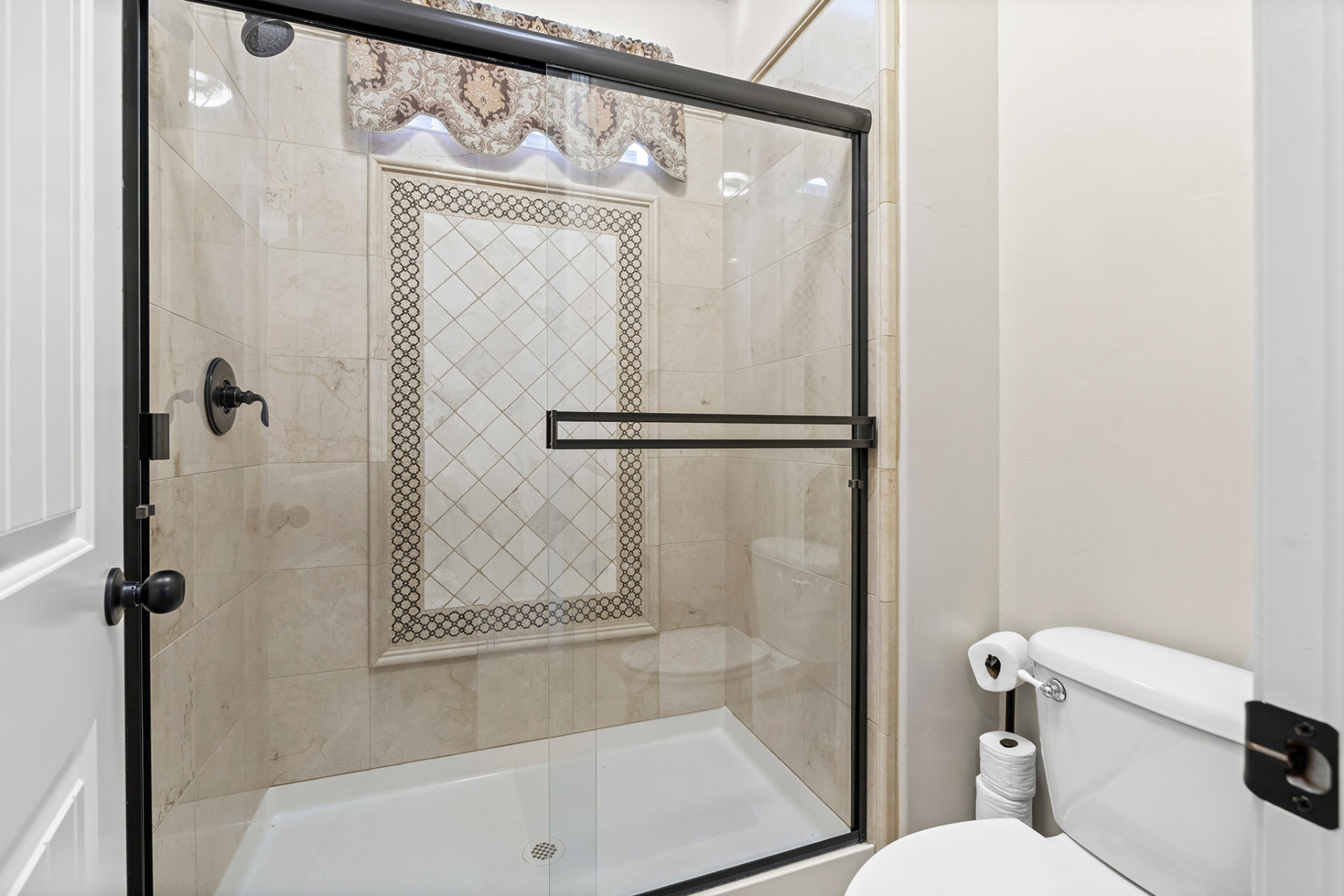 Guest bath tiled tub-shower with a decorative stone inlay