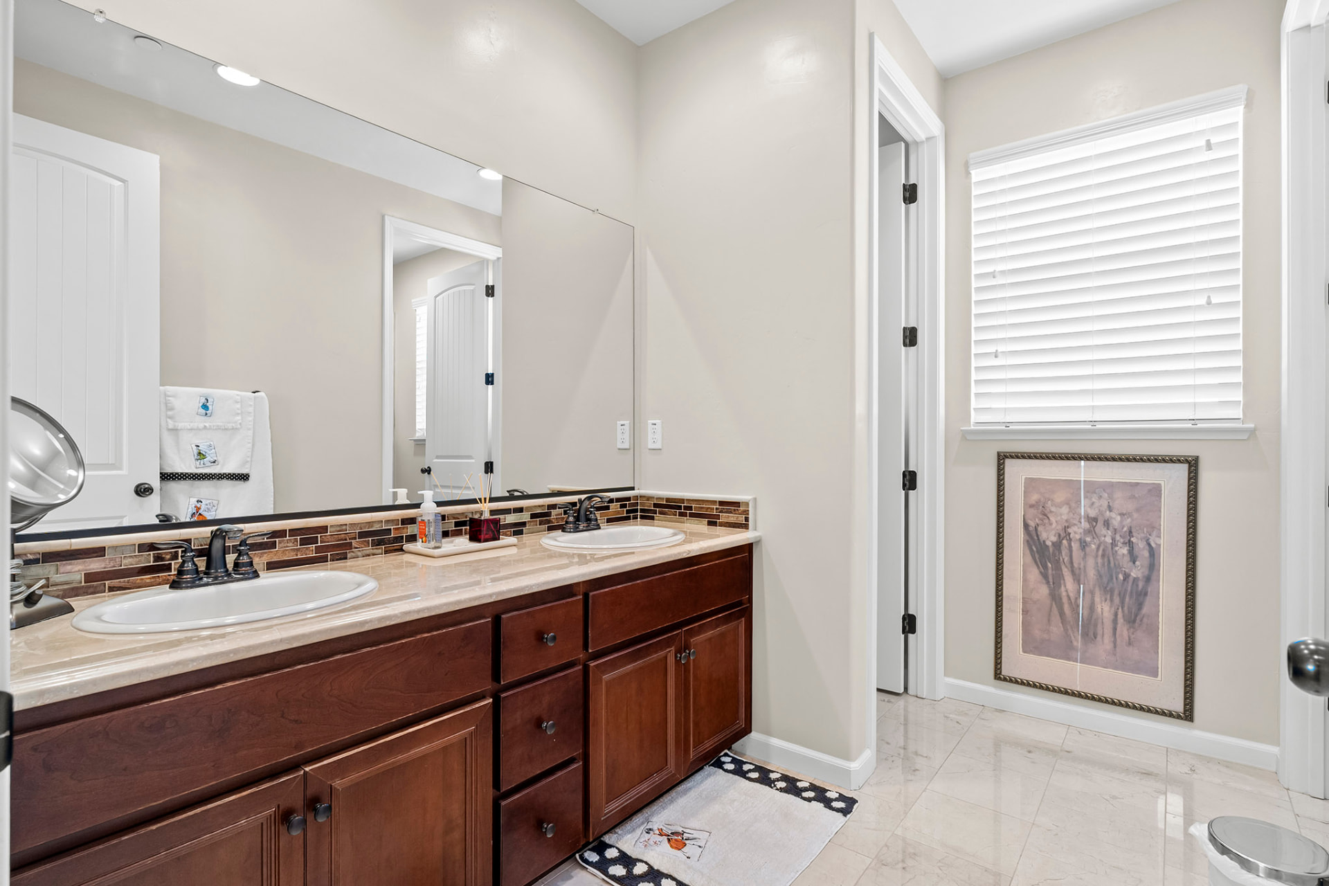 Full bath with a dual-sink vanity, mosaic backsplash, and marble-look tile floor