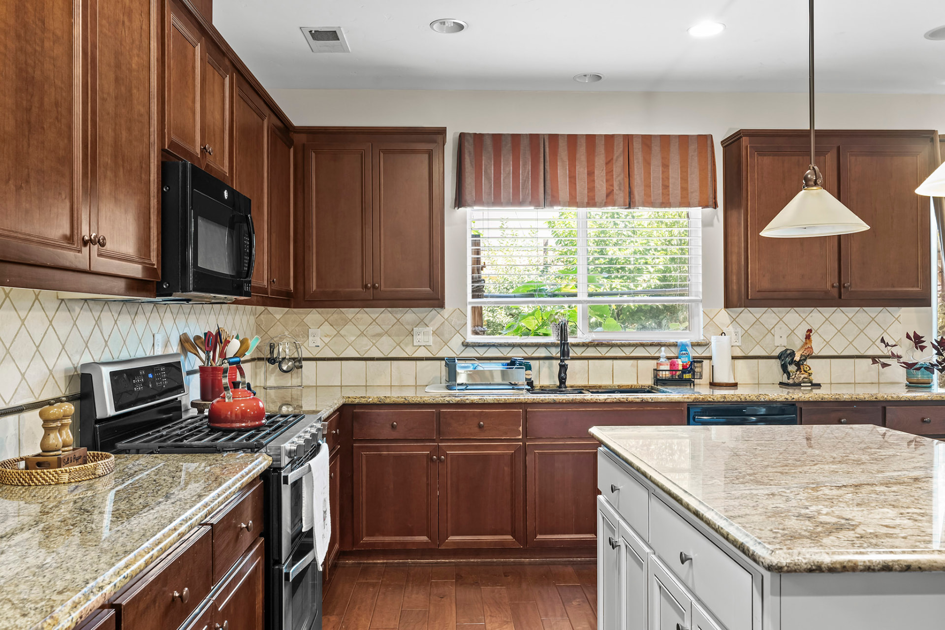 Kitchen range and granite counters with a tile backsplash and garden window view
